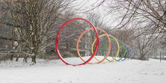 Die bunte Spektralringe aus Stahl stehen auf einer schneebedeckten Wiese auf dem Campus Nord.