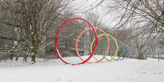 Die bunte Spektralringe aus Stahl stehen auf einer schneebedeckten Wiese auf dem Campus Nord.
